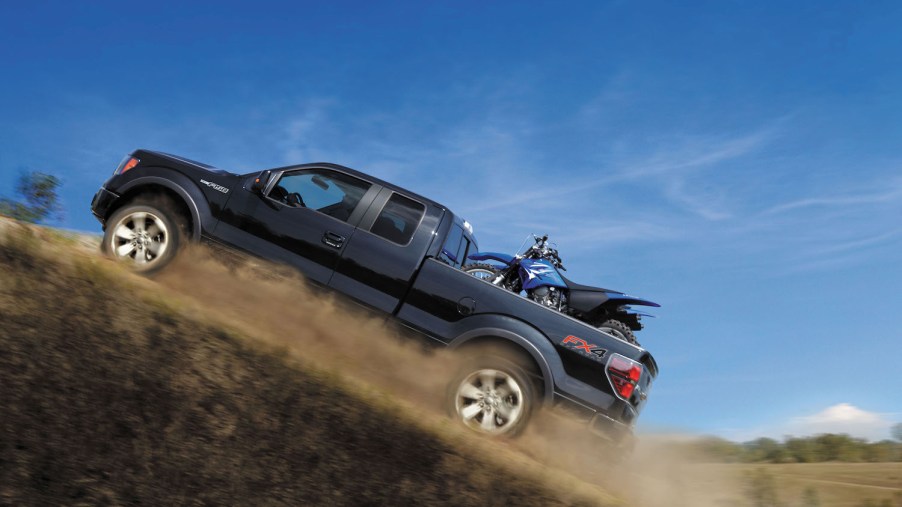 Promo photo of a 2014 Ford F-150 half-ton 4x4 pickup truck climbing a steep hill with a dirt bike in its bed, a blue sky visible in the background.
