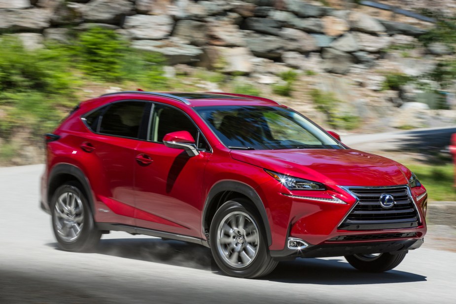 Red hybrid Lexus NX 300 luxury crossover SUV rounding a bend in a mountain road, stones and plants visible in the background.