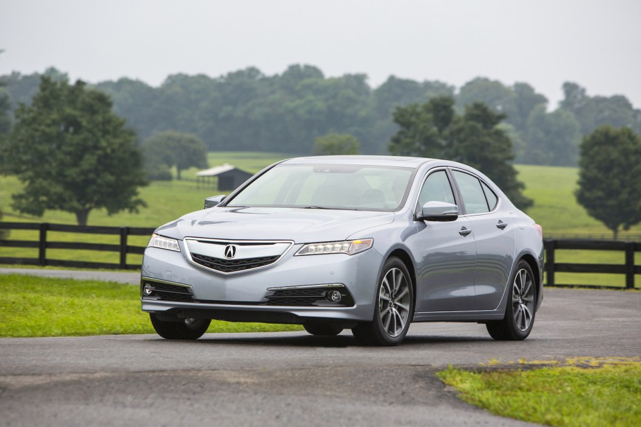 Silver 2015 Acura TLX driving past a fence in the countryside for a promo photo.