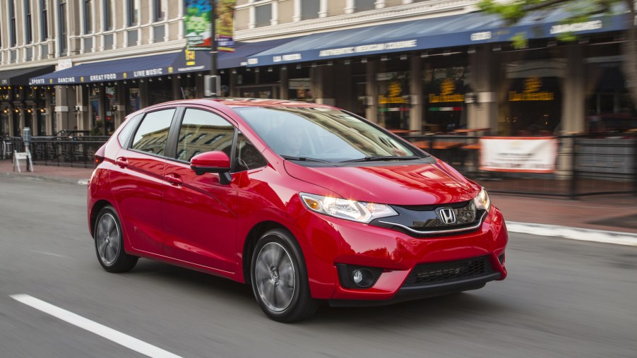 A red 2016 Honda Fit driving down a city street