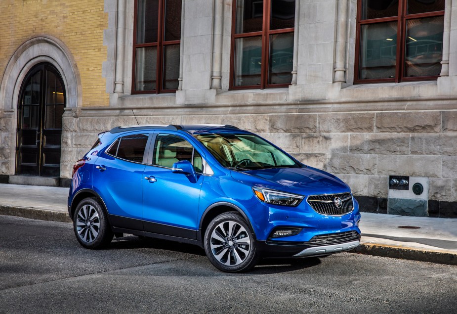 Bright blue Buick Encore crossover SUV parked in front of a marble stone building for a promo photo.