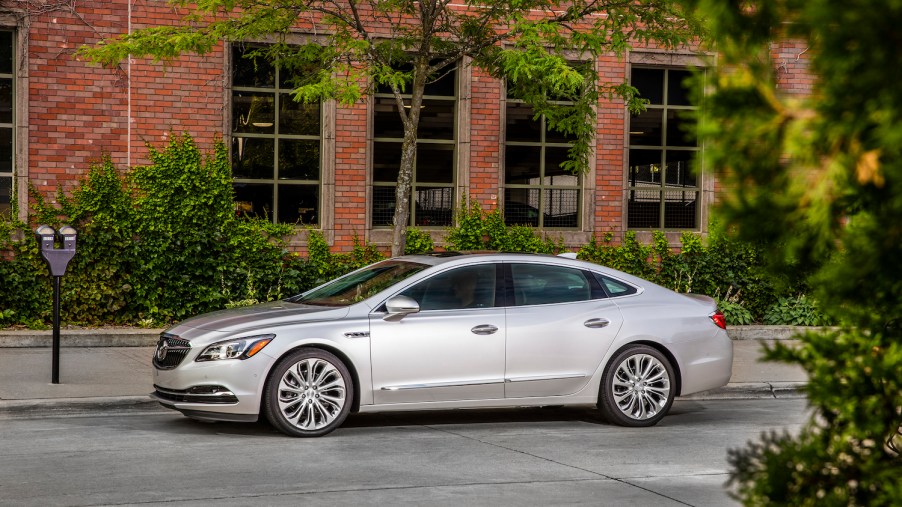 Silver Buick LaCrosse sedan parked in front of a brick wall, leaves visible in the foreground.