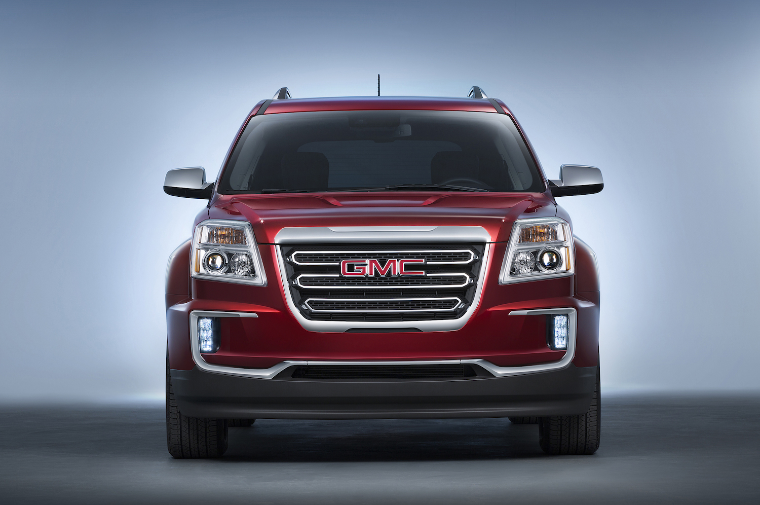 Publicity photo of the large, chrome grille of a red GMC Terrain crossover SUV parked in a studio, a white background behind it.