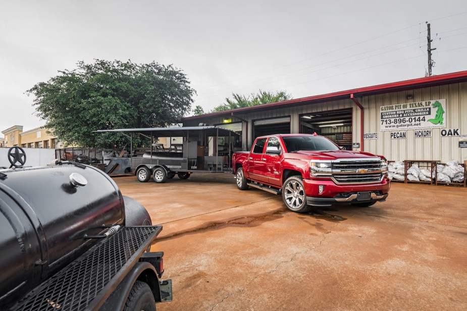 Used 2018 Chevrolet Silverado 1500 half-ton parked in front of a garage, a trailer hooked up to its hitch.