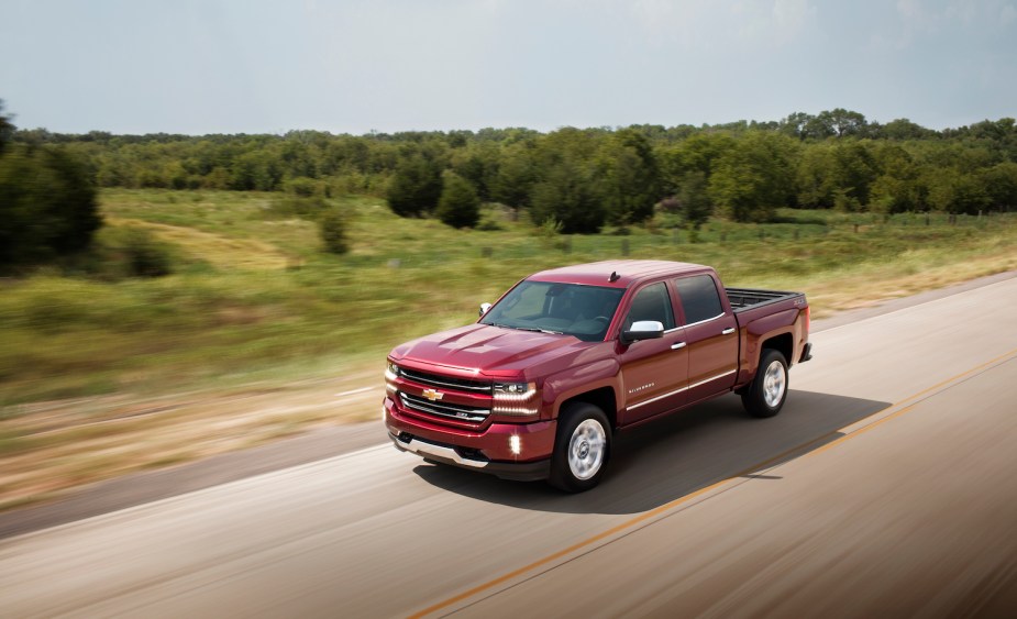 A full-size red Chevrolet Silverado 1500 pickup truck drives down a paved road, trees blur in the background.