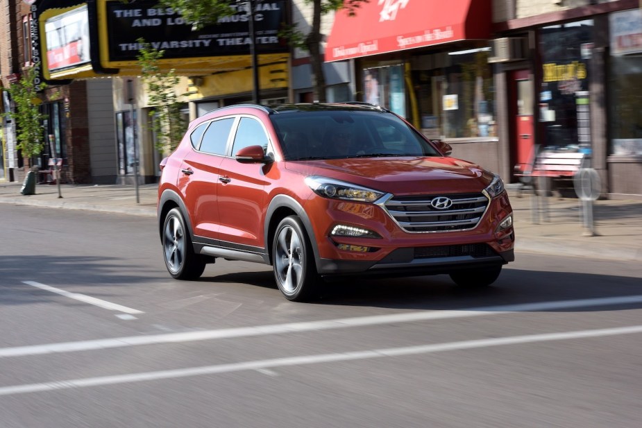 A red Hyundai Tucson driving down a city street, storefronts visible in the background.