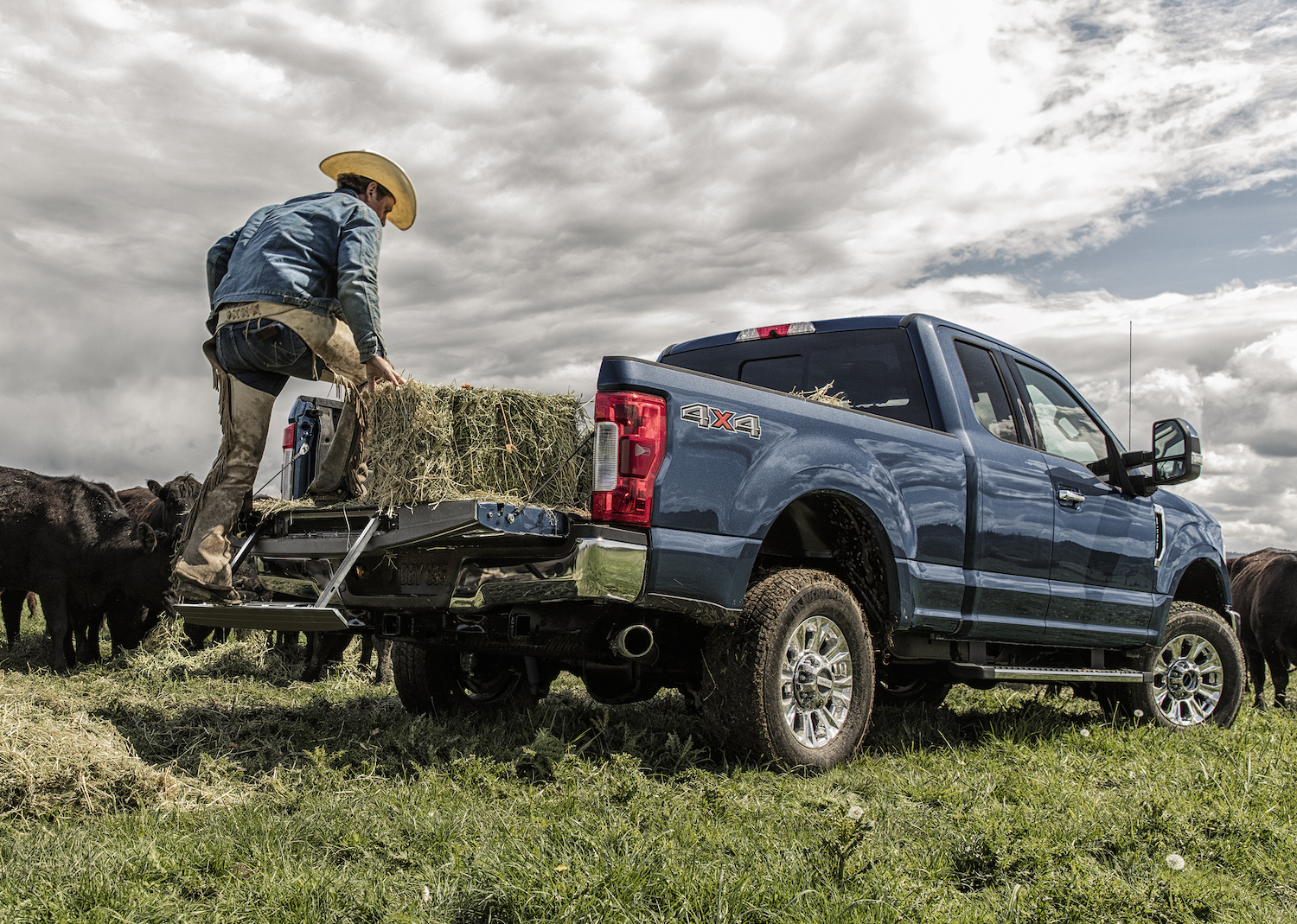 A man loading a hay bale into the bed of a blue Ford Super Duty pickup truck.