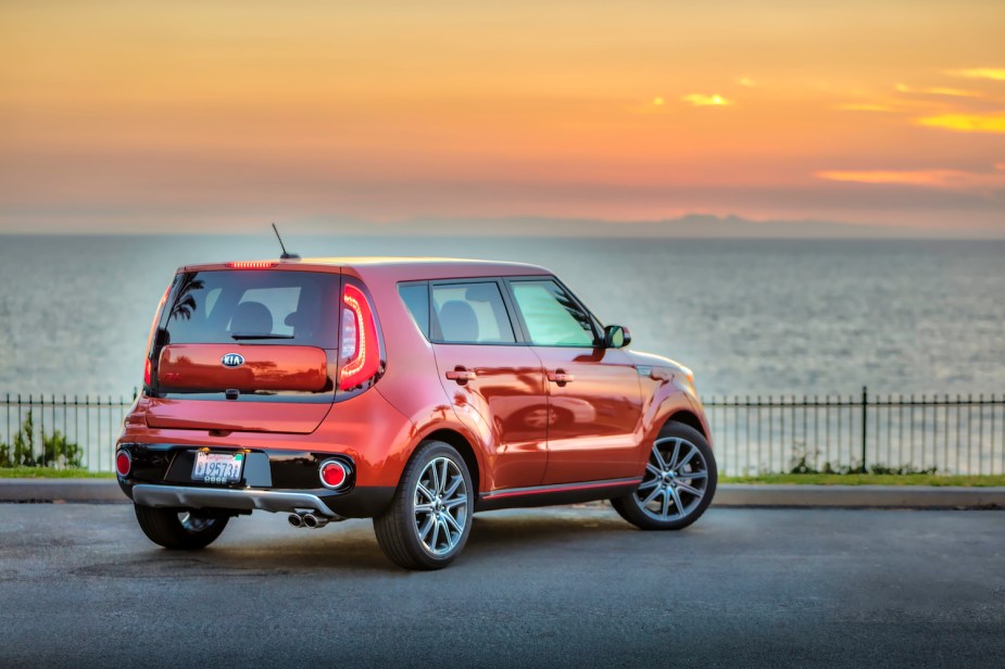 A red 2019 Kia Soul crossover SUV facing away from the camera as the sun sets over a lake in the background.