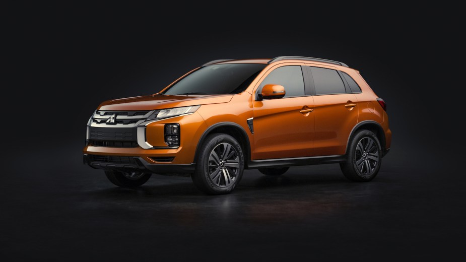 An orange 2020 Mitsubishi Outlander crossover SUV parked in front of a black studio background for a publicity photo.