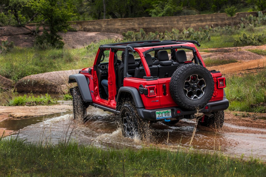 A red Jeep Wrangler 4xe driving through a river while off-roading with its top down.