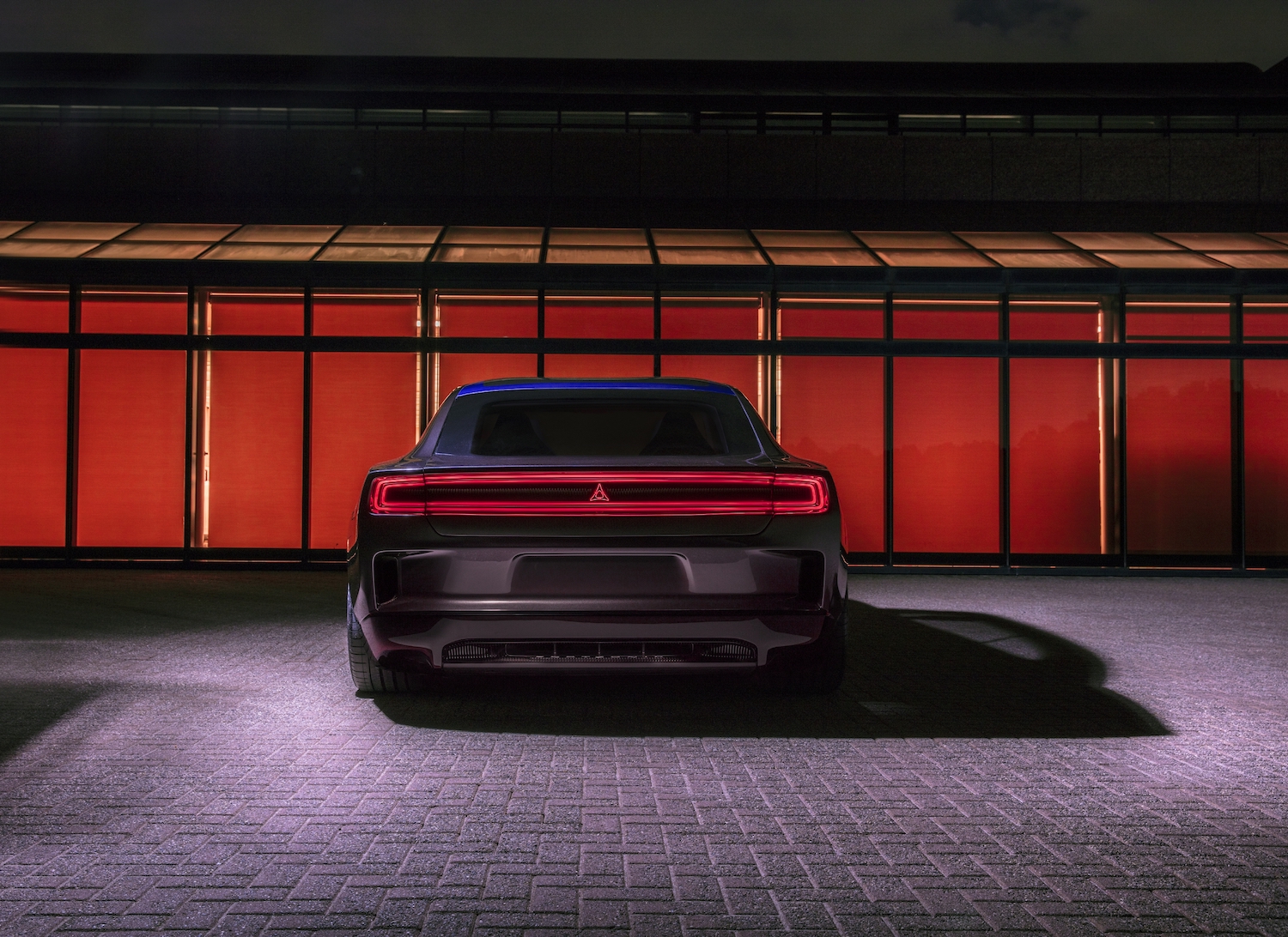 A Dodge Charger Daytona SRT Banshee EV concept car parked in front of a red, glowing window.