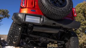 An orange 2022 Ford Bronco Wildtrak off-road SUV model with option HOSS 3.0 climbing over a hill of rocks