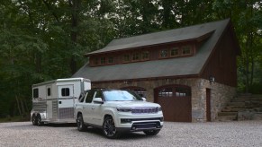 2022 Grand Wagoneer in white towin g a horse trailer by a farm.