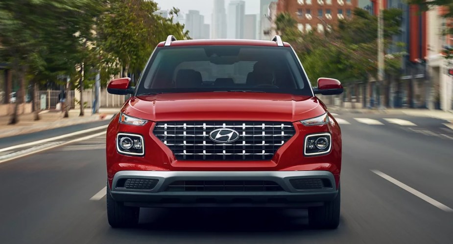 A red 2022 Hyundai Venue subcompact SUV is driving on the road. 