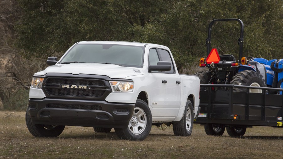 A white Ram 1500 tradesman work truck hooked up to a trailer with a tractor on top of it.