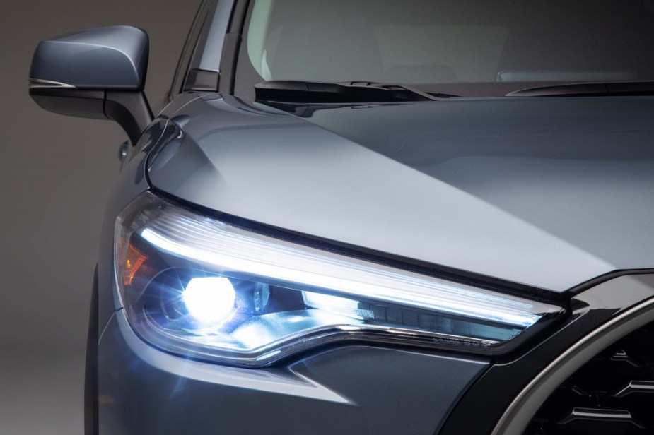 The headlight of a silver 2022 Toyota Corolla Cross a Toyota SUV with the best gas mileage. 