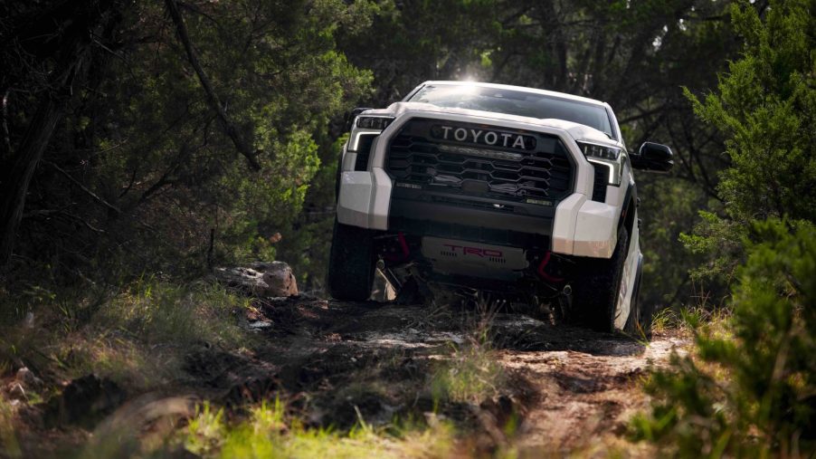 A white 2022 Toyota Tundra TRD Pro pickup truck navigates an off-road 4x4 trail, trees in the background.