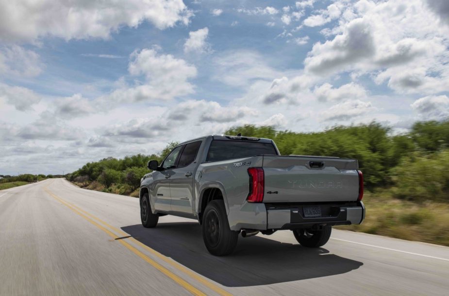 The tailgate of a 2022 Toyota Tundra SR5 pickup truck as it drives down a country road, trees in the background.