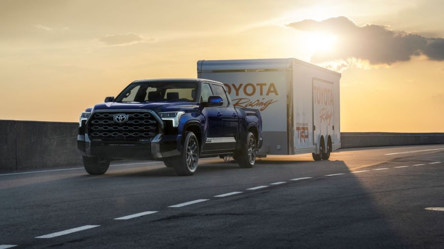 A dark blue 2022 Toyota Tundra full-size pickup truck towing a Toyota Racing trailer on a highway at sunset