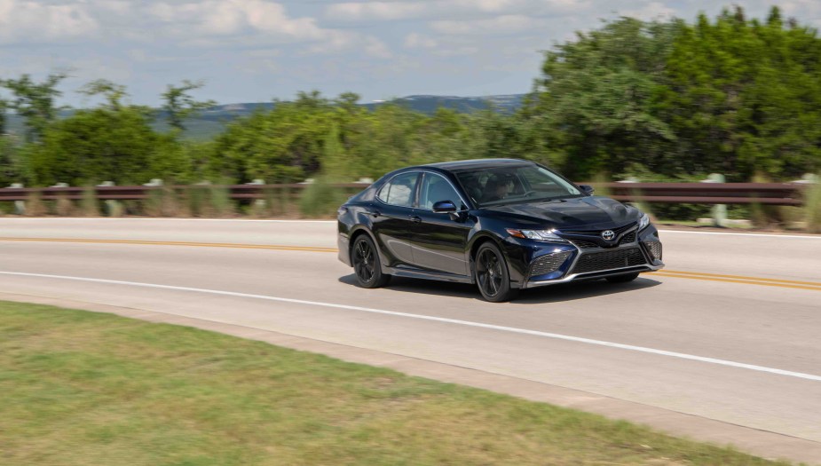 The 2022 Toyota Camry XSE is shown driving down a treelined road facing right