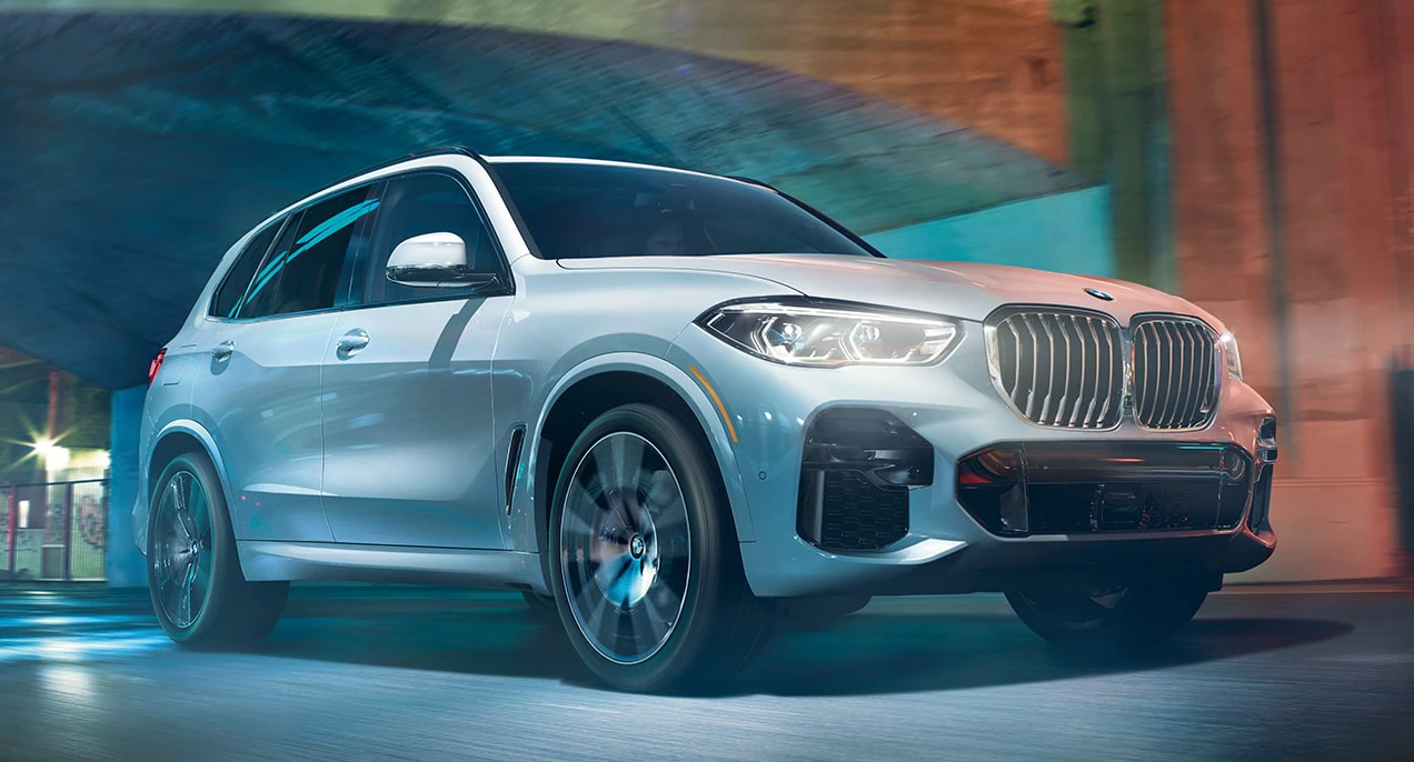 A white 2023 BMW X5 luxury midsize SUV is driving on the road.