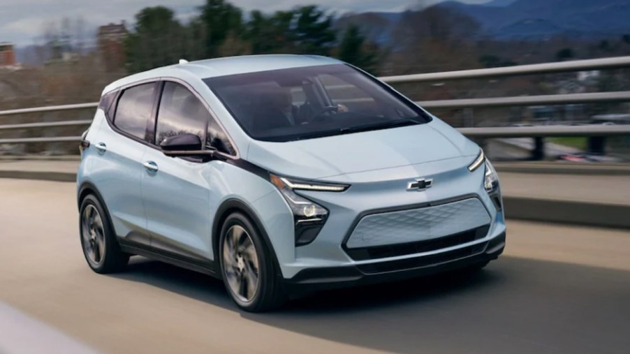 A blue 2023 Chevy Bolt EV electric hatchback is driving on the road.