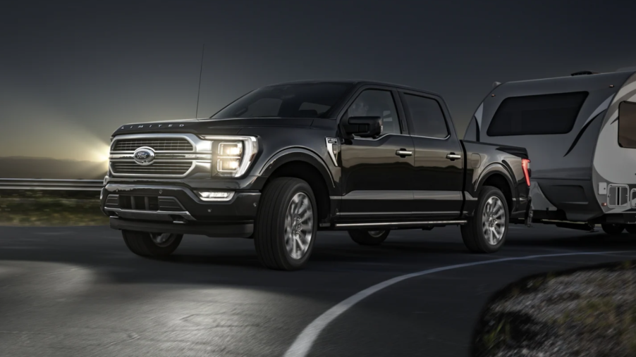 A black 2023 Ford F-150 full-size pickup truck with LED fog lamps towing a camper at night