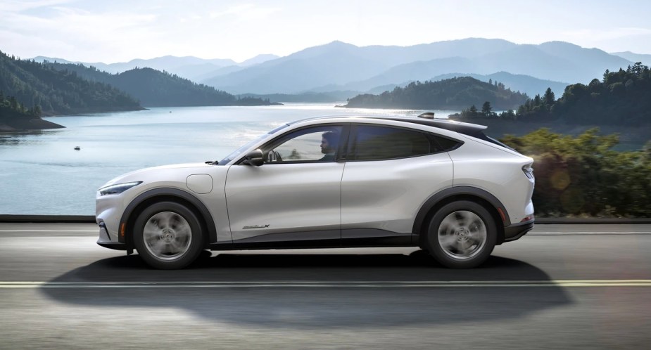 A white 2023 Ford Mustang Mach-E small electric SUV is driving on the road. 