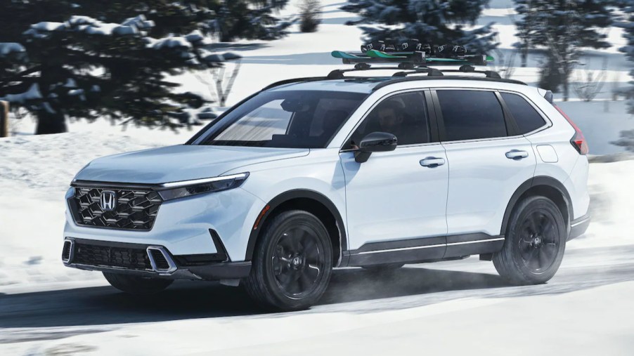 A white 2023 Honda CR-V Hybrid small hybrid SUV is driving in the snow.