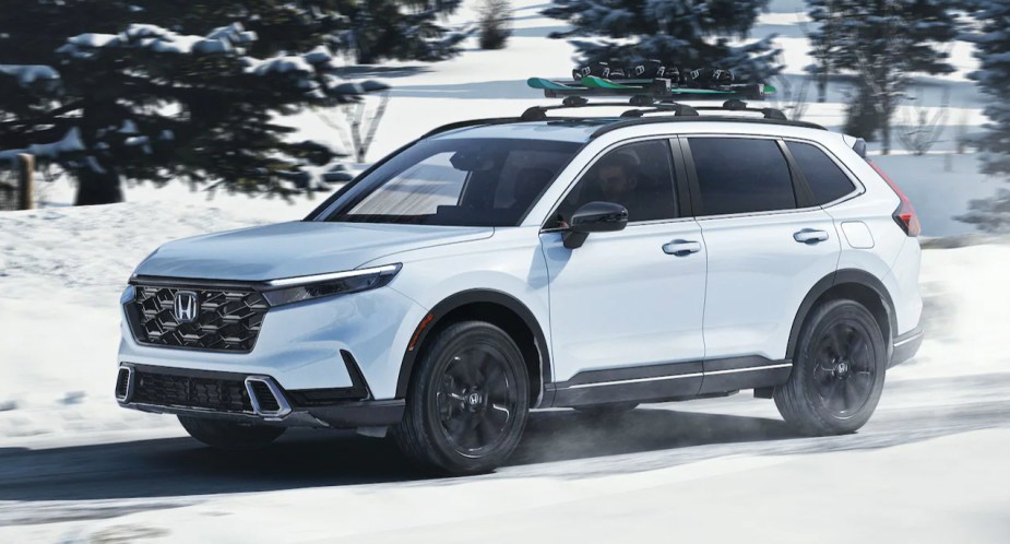 A white 2023 Honda CR-V Hybrid small hybrid SUV is driving in the snow.