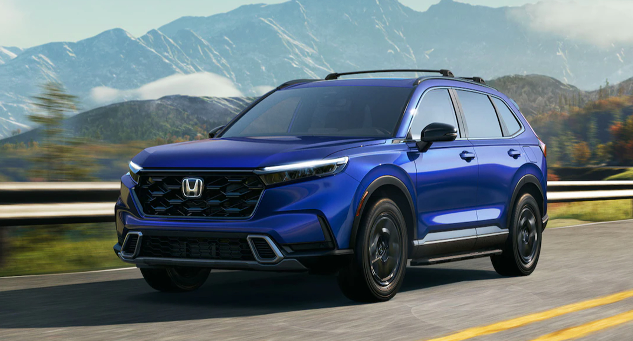 A blue 2023 Honda CR-V Hybrid small SUV is driving on the road.