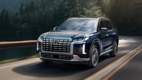 A blue Hyundai Palisade midsize SUV is driving on the road.