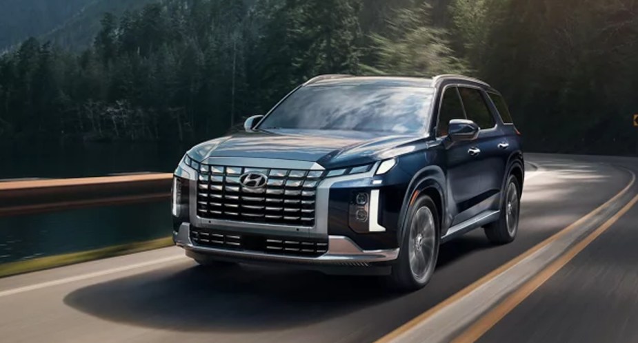 A blue Hyundai Palisade midsize SUV is driving on the road.