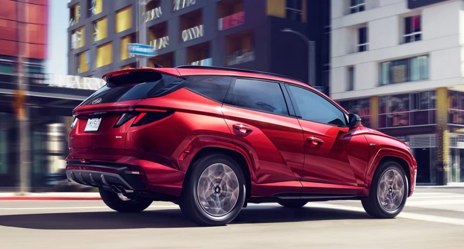 A red 2023 Hyundai Tucson small SUV is driving on the road. 