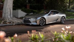 A silver gray 2023 Lexus LC 500h hybrid luxury sports car model parked under the shade of a white bark tree