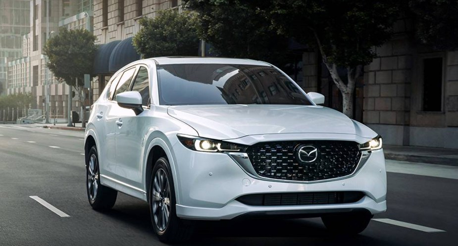A white 2023 Mazda CX-5 small SUV is driving on the road. 
