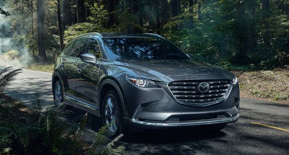 A gray 2023 Mazda CX-9 midsize SUV is driving on the road. 