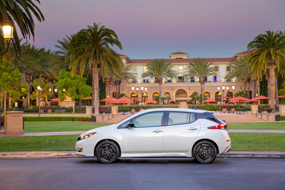 A white 2023 Nissan Leaf in front of a building in a tropical area. 