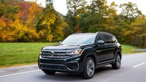 A 2022 Volkswagen Atlas full-size SUV model driving on a highway near trees with autumn-colored leaves