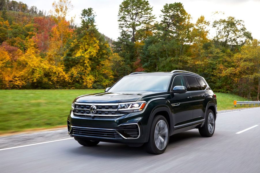 A 2022 Volkswagen Atlas full-size SUV model driving on a highway near trees with autumn-colored leaves