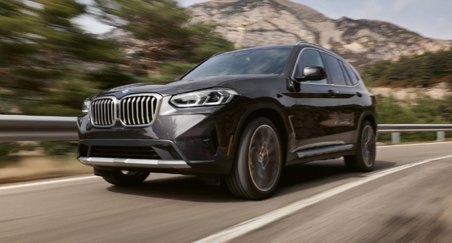 A gray 2023 BMW X3 small luxury SUV is driving on the road. 