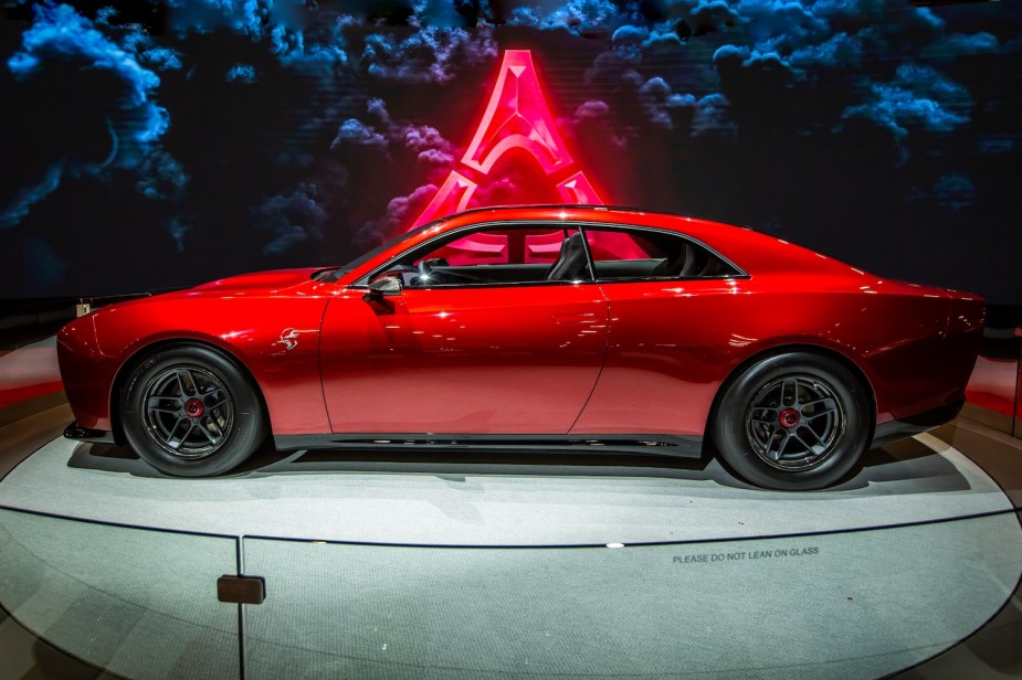 The profile of Dodge's eMuscle concept, the Charger Daytona, parked on a stage at an auto show, a fratzog symbol in the background.