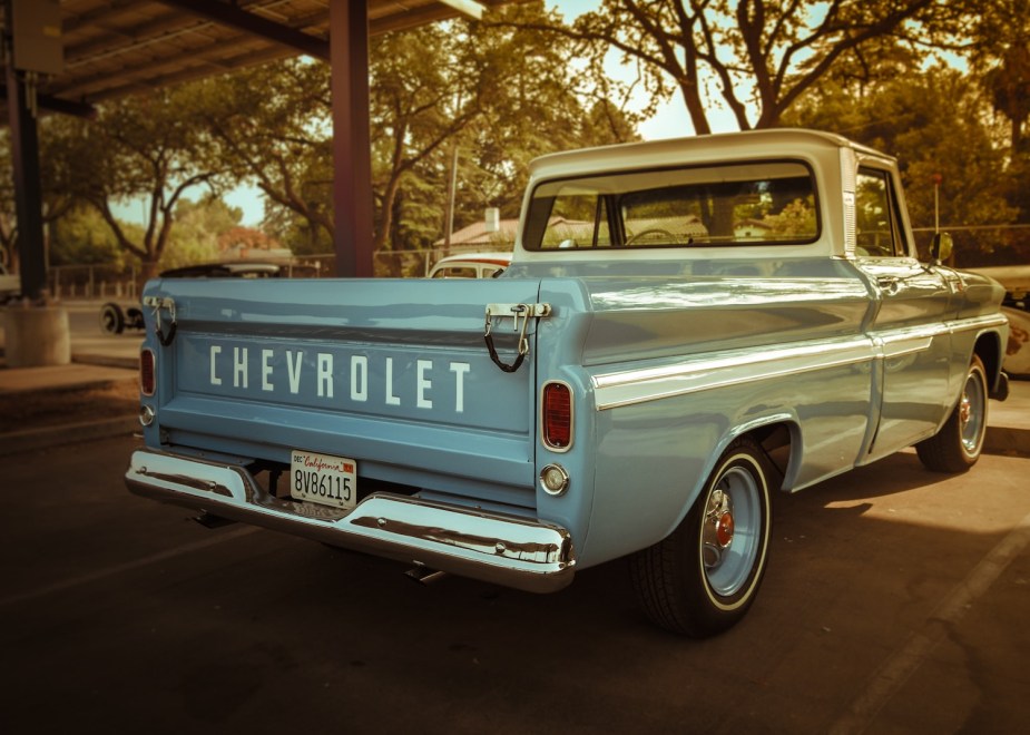 The bed of a blue colored Chevrolet fleetside classic pickup truck, trees visible in the background.