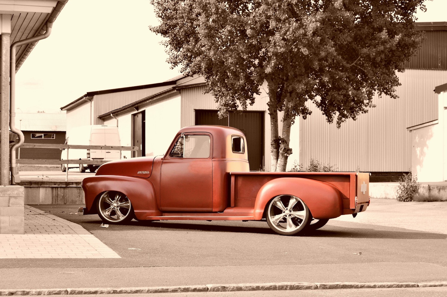 A classic red Chevrolet pickup truck parked in front of a tree, in a parking lot.