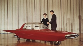 A couple stands next to the 1961 Ford Gyron concept car on stage at the Detroit auto show, a white curtain visible behind them.