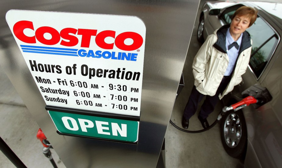 The hours of operation sign at a Costco gas station, a customer pumping in the gas visible in the background.