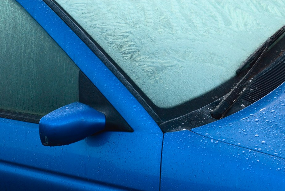 Closeup of a blue car with its windshield covered in ice crystals.
