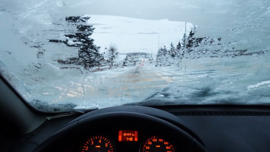 The view of a snowy winter road through a partially defrosted car windshield.