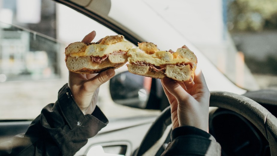Driver holding a bagel sandwich, highlighting how to eat in a car without making a mess