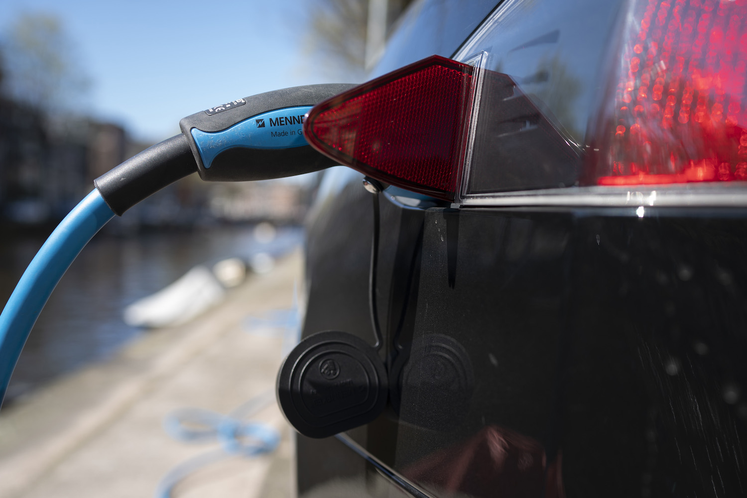 Un câble de recharge de véhicule électrique bleu de rechange branché sur le port d’une Tesla, l’aile noire et le feu arrière de la voiture électrique visibles au premier plan.